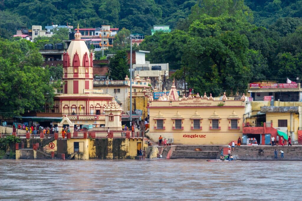 Vibrant scene at Ganga Ghat, Rishikesh with temple and riverfront in view.